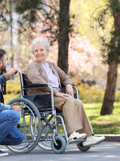 Senior woman in wheelchair with young man at park