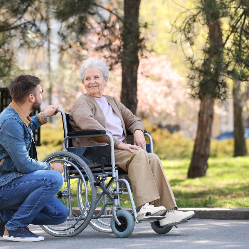 Senior woman in wheelchair with young man at park