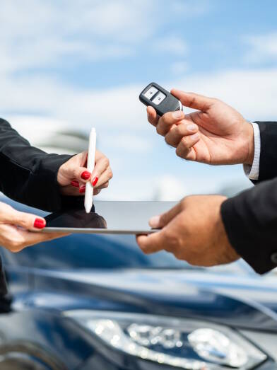 Young businesswoman renting a car with sale manager signing deal on tablet getting key and go to driving car. Buy sell rent concept. Hand sending key vehicle contract car deal