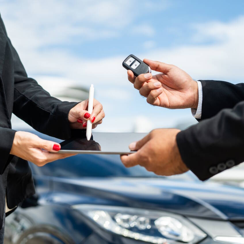 Young businesswoman renting a car with sale manager signing deal on tablet getting key and go to driving car. Buy sell rent concept. Hand sending key vehicle contract car deal